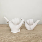 two white bonded marble ring holders with the hang ten or roadrunner hand signal. One with base, one without.