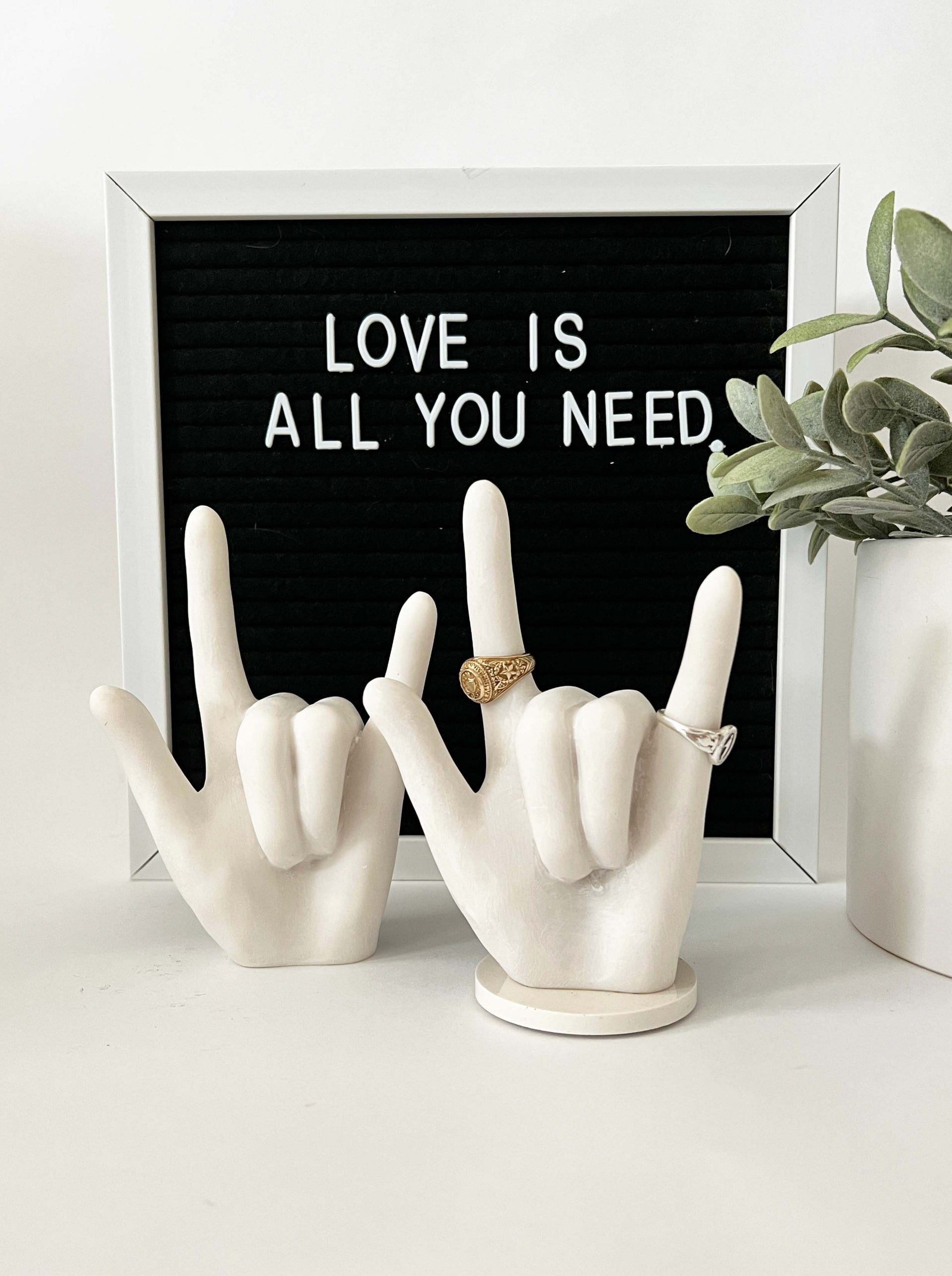 White bonded marble ring holder signaling I Love You in ASL.